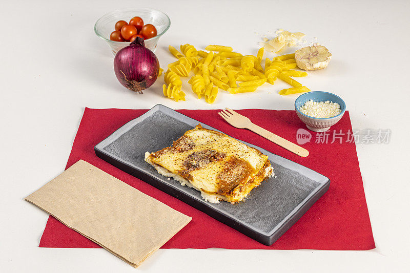 Fine veal lasagna with cheese and béchamel gratin on a black plate and red tablecloth